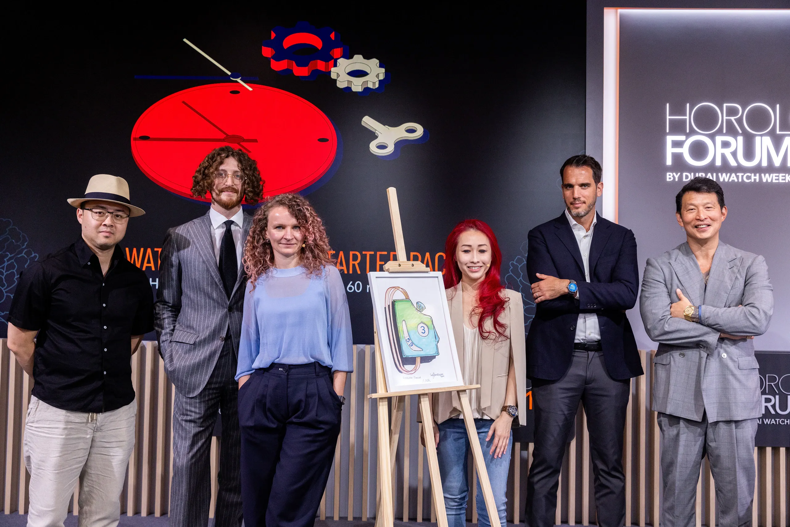 Speakers posing on the Horology Forum 10 stage beside an illustrated easel